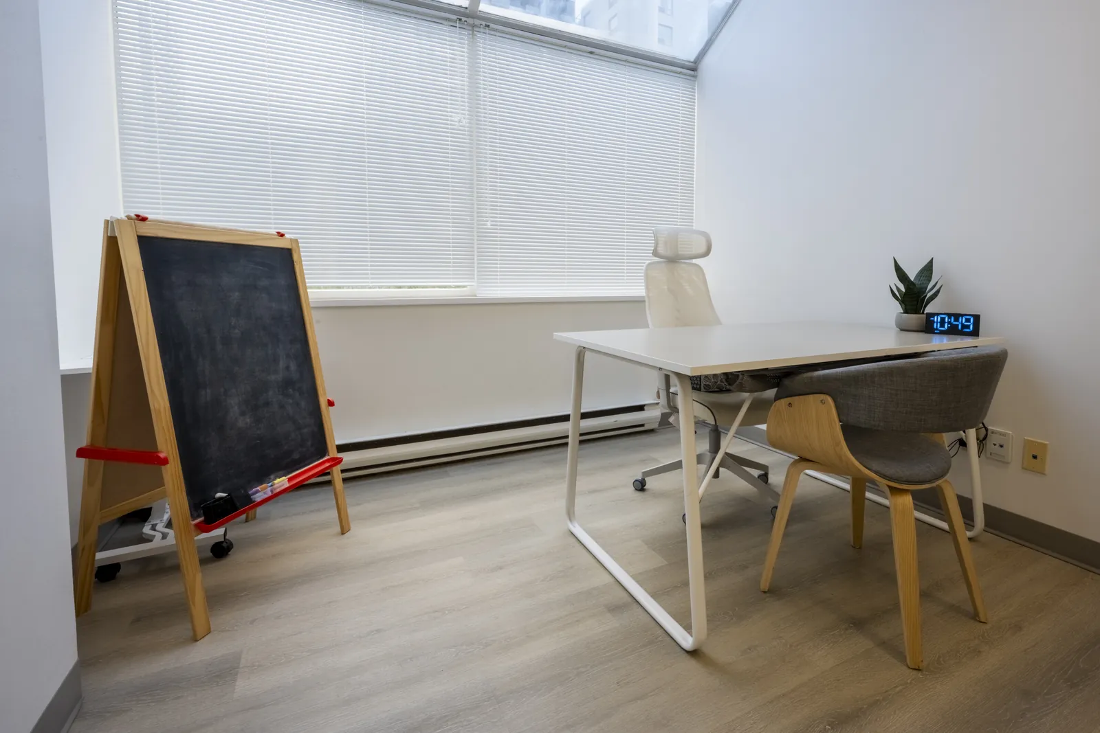 Therapy room with a chalkboard easel for younger clients, a desk and window blinds