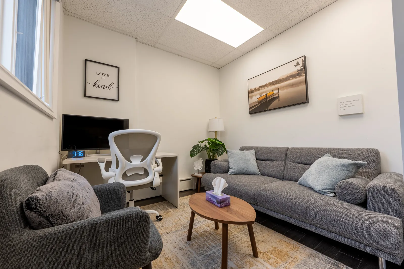 Small therapy room with a grey armchair, a sofa with light blue cushions and a wooden coffee table