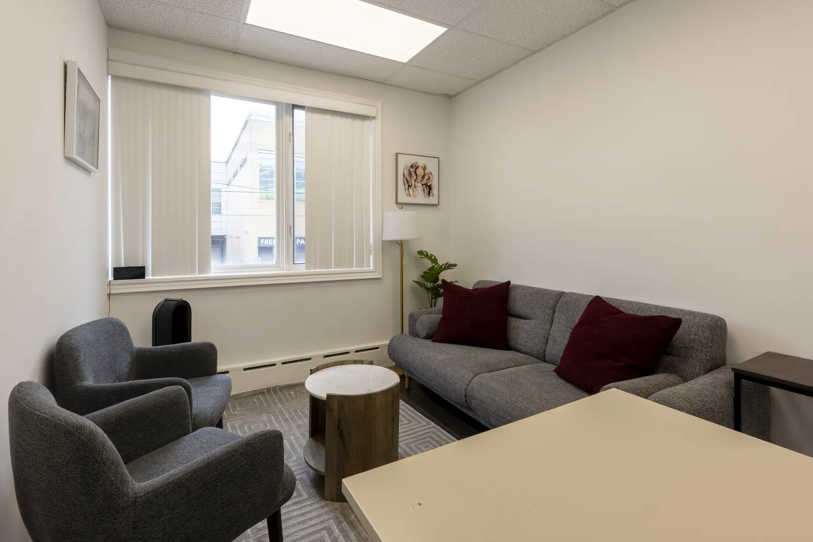 Therapy room with two grey armchairs, a sofa with burgundy cushions and a marble side table