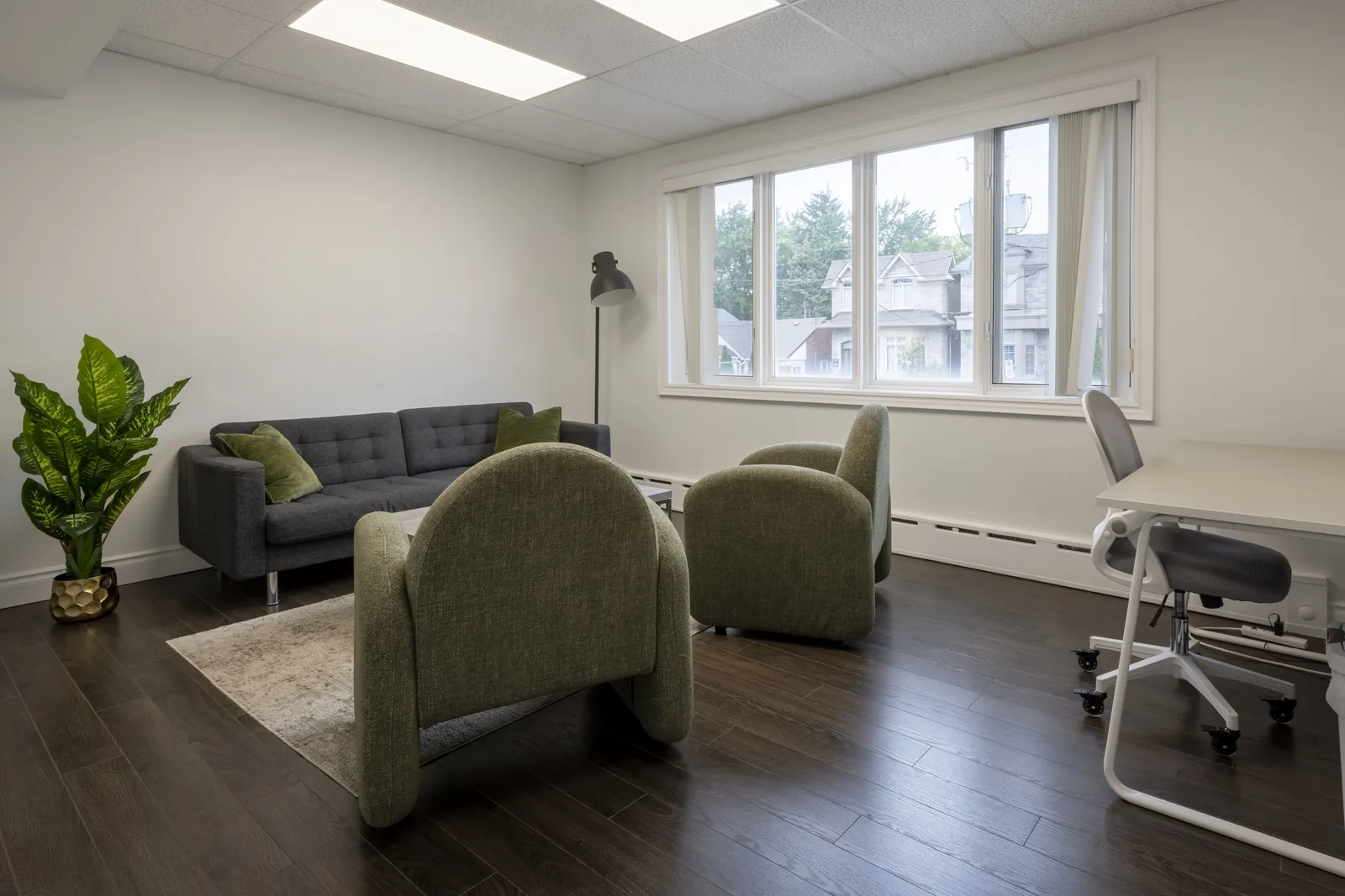 Large therapy room in North York with green armchairs, a dark grey sofa and a window looking onto nearby houses