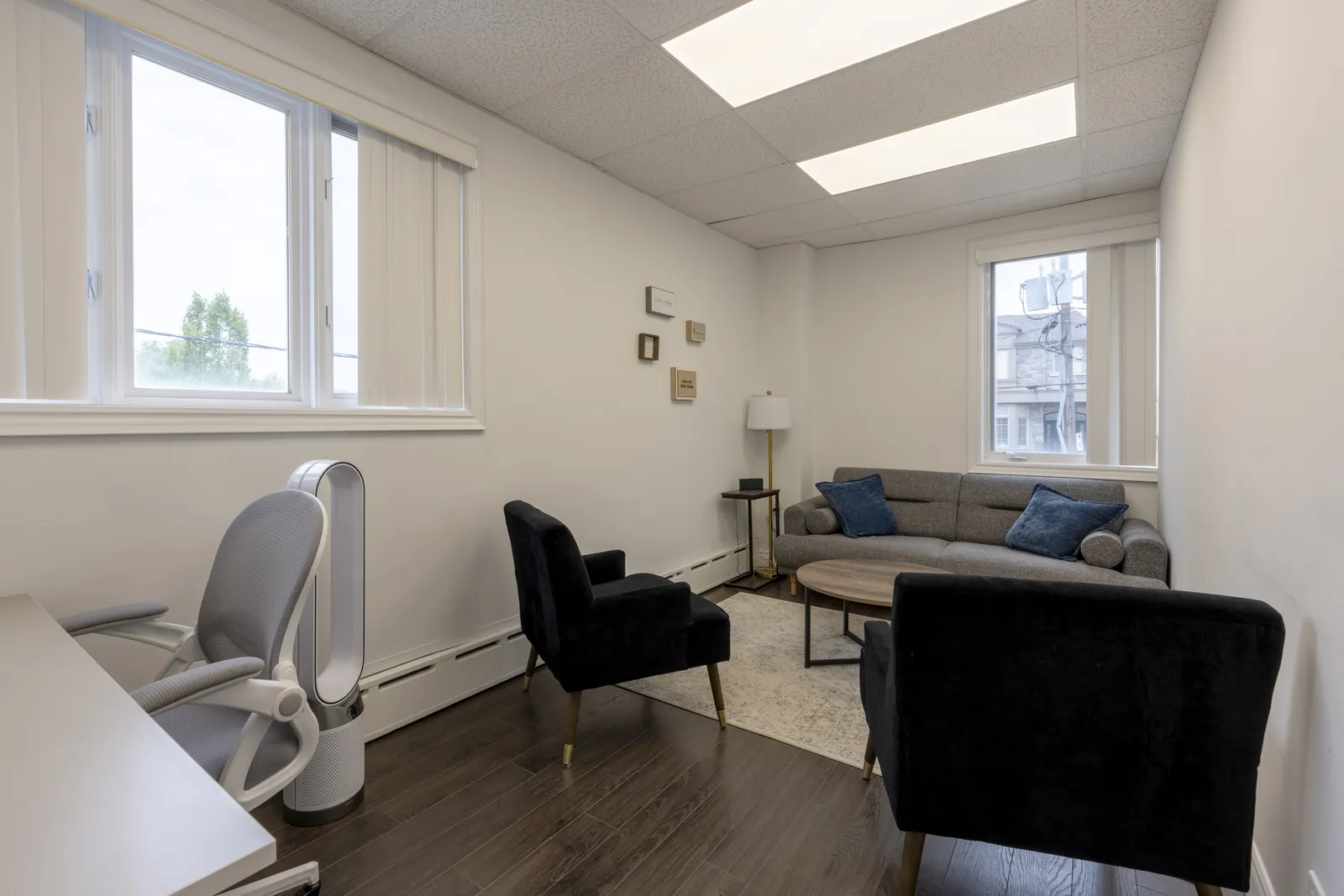 Therapy room with navy armchairs, a grey sofa with navy cushions and two windows