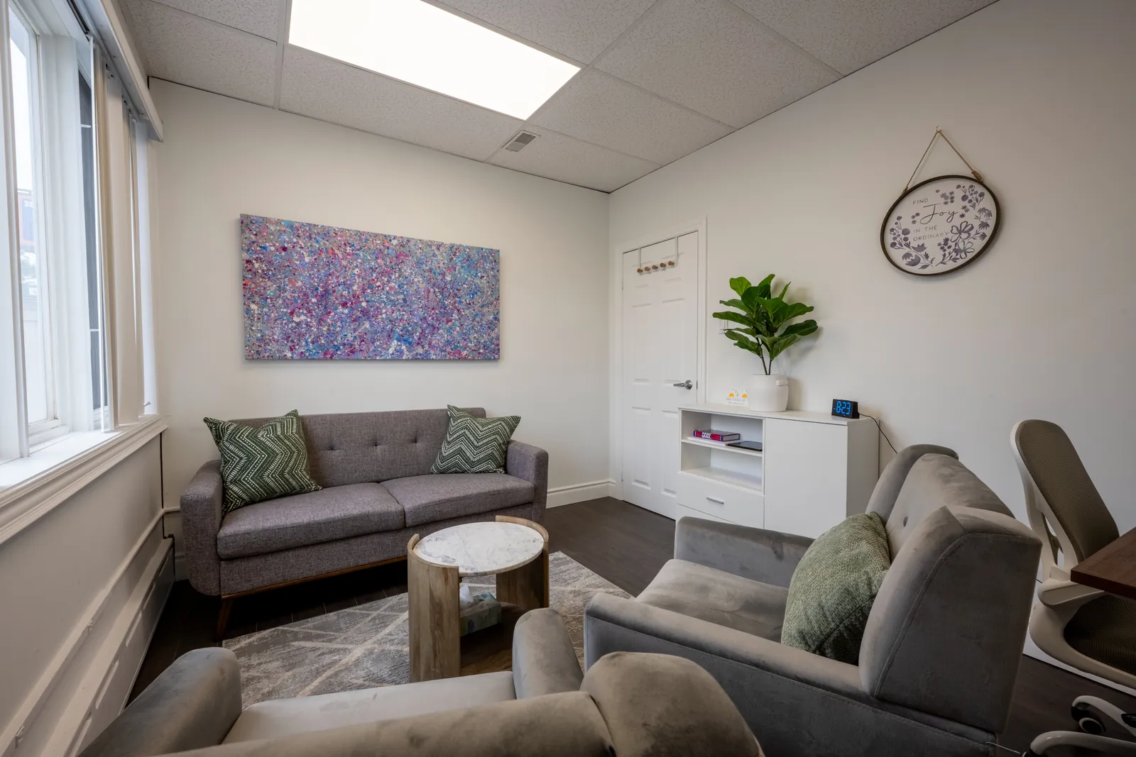 Therapy room with grey velvet armchairs, a grey sofa and an abstract painting in blue and pink